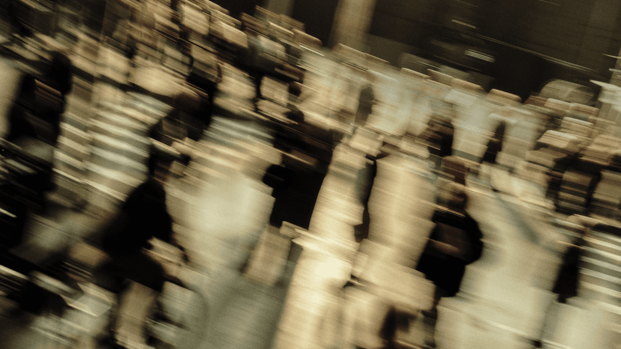 Heavily motion-blurred image of pedestrians walking, their forms streaked diagonally into abstract shapes of light and shadow.