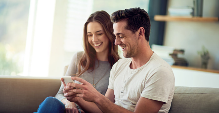 Smiling couple on couch looking at phone