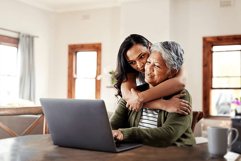 woman hugs older woman as she uses laptop computer