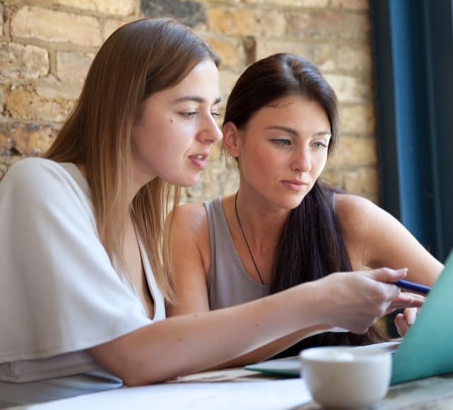 Two young women pointing at screen questwealth